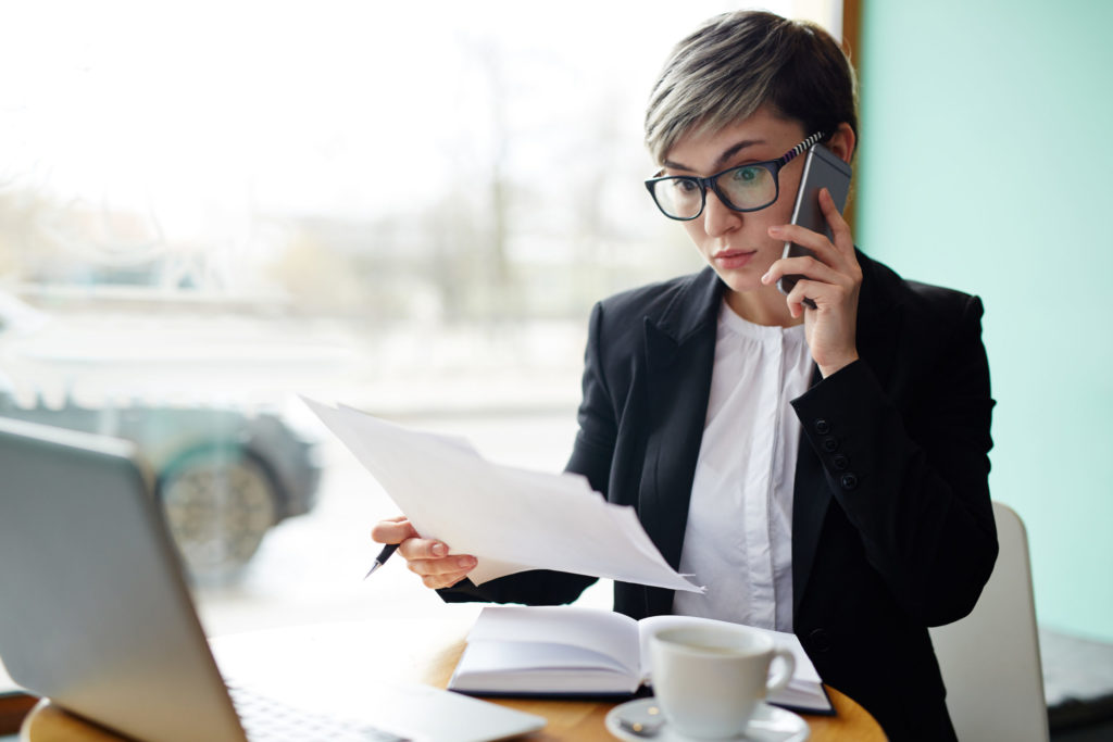 Astonished woman looking at document while talking on cellphone